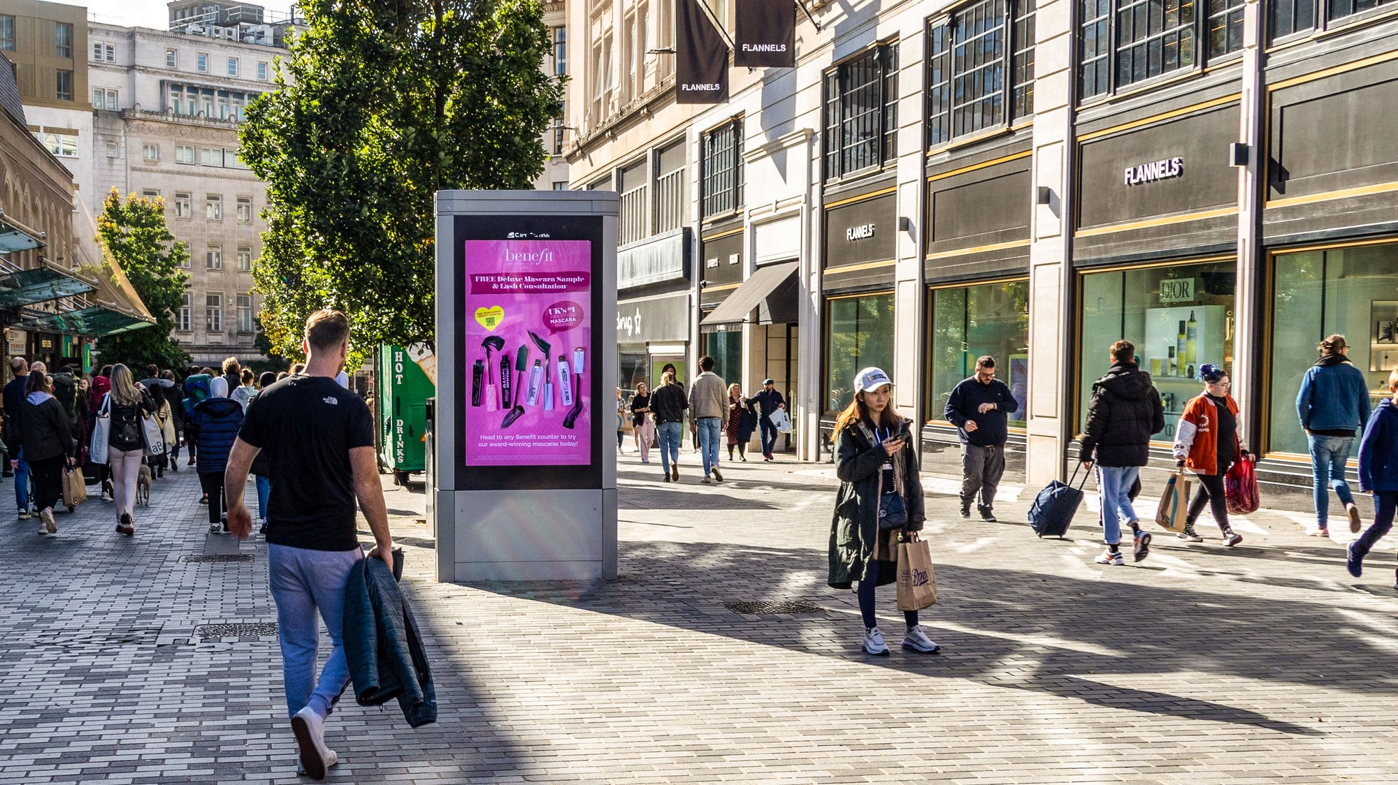 Adshel Live screen in Glasgow displaying Benefit Cosmetics ad campaign with people walking past